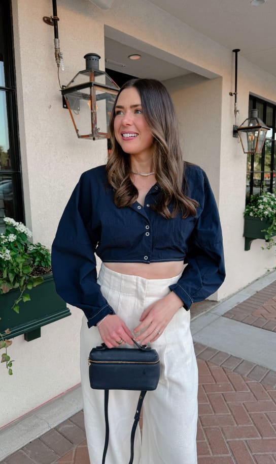 Maddy wearing a navy cropped top and white trousers outside a café