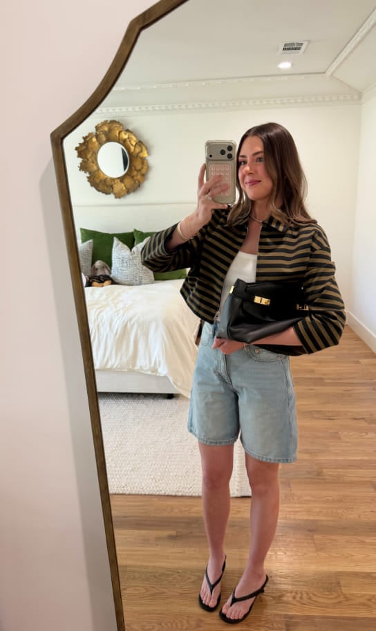 Maddy taking a mirror selfie in a striped jacket and denim shorts