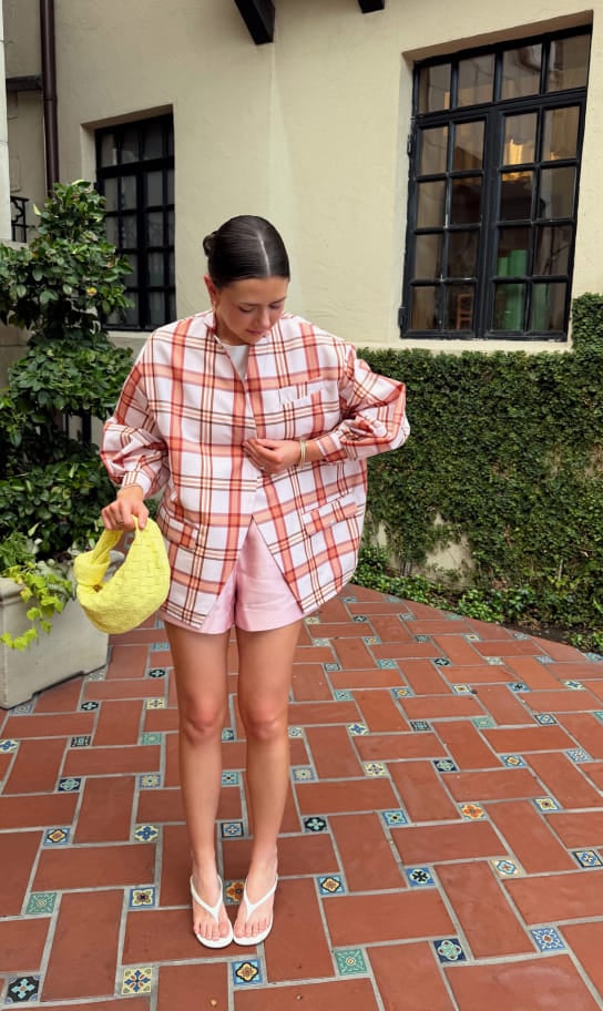 Maddy wearing an oversized plaid shirt and pink shorts on a tiled patio