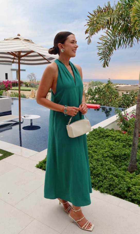 Maddy wearing a green halter maxi dress poolside at sunset