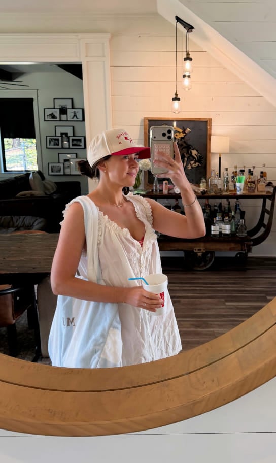 Maddy taking a mirror selfie in a white ruffled dress and baseball cap