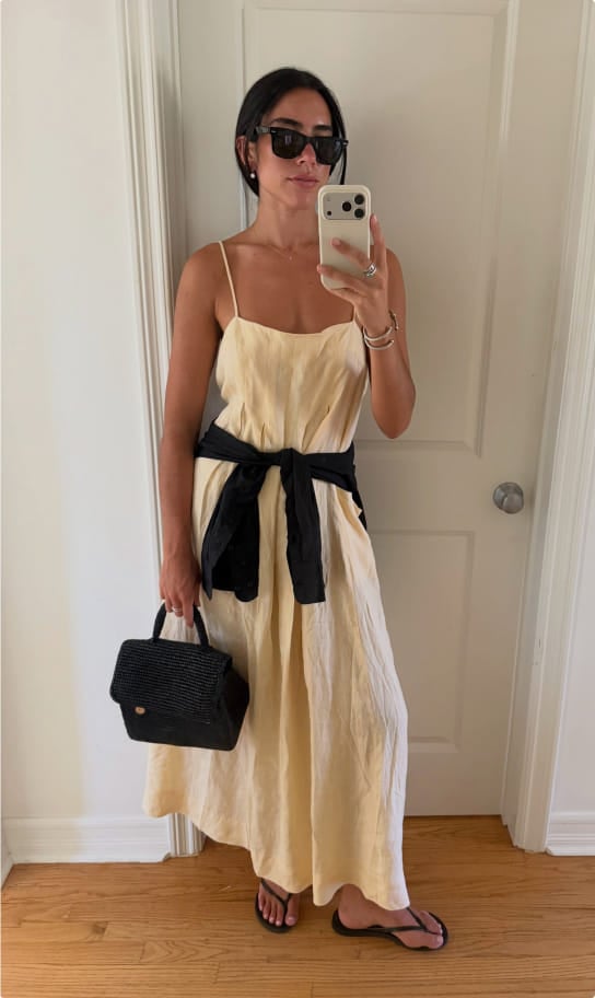 Ceci in a cream slip dress with a black sash, holding a black bag