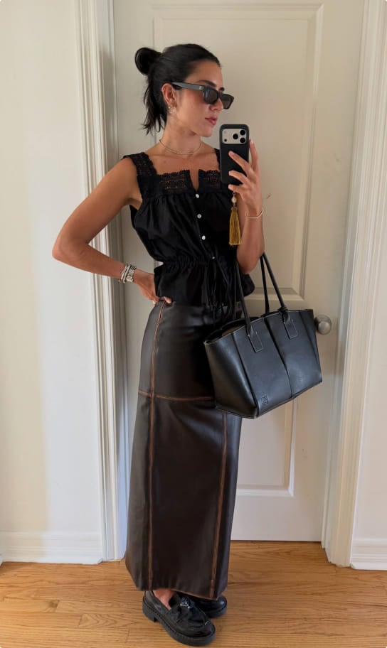 Ceci in a black ruffled top and brown leather midi skirt, holding a black tote
