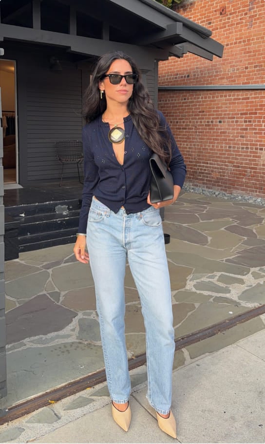 Ceci in a navy shirt and light-wash jeans standing outside a brick building