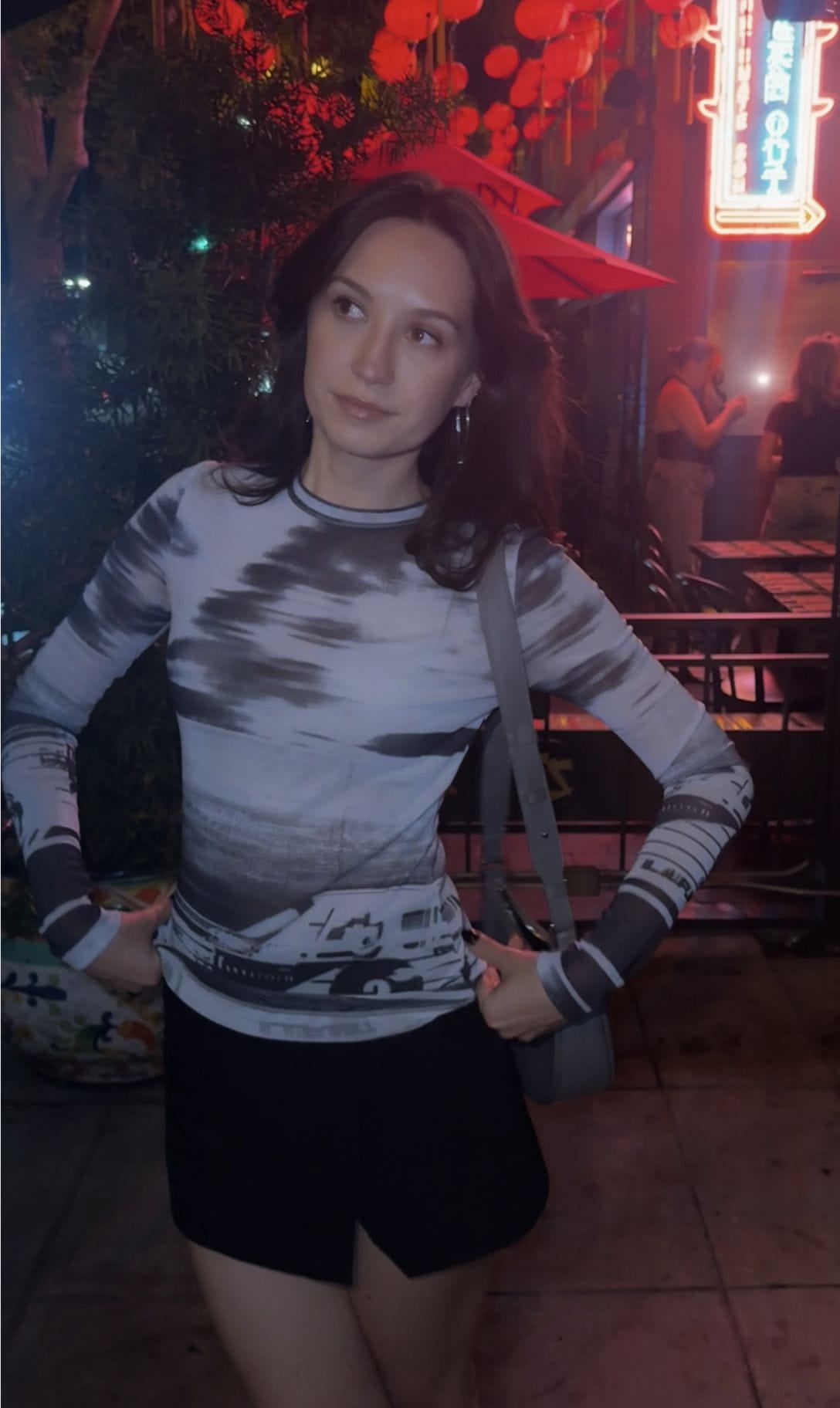 Aleksandra wearing a graphic long-sleeve top and black skirt at night